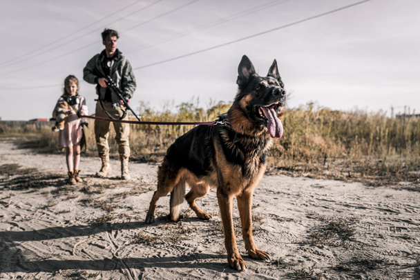 selective focus of german shepherd dog near armed man and kid, post apocalyptic concept - Photo, Image
