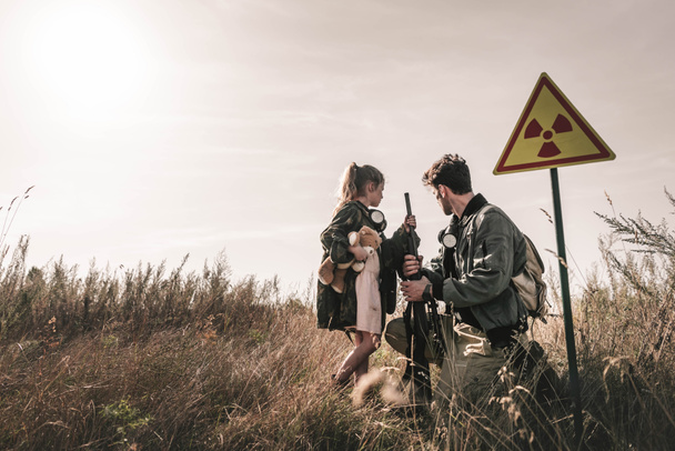 handsome man with gun near kid with teddy bear and toxic symbol, post apocalyptic concept - Photo, Image