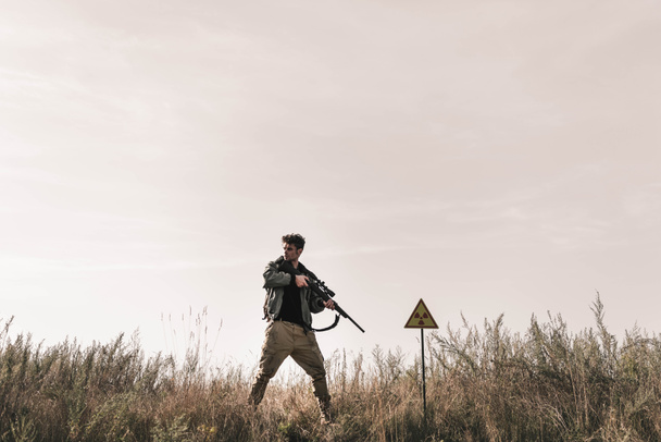  man holding gun near toxic symbol in field, post apocalyptic concept - Photo, Image
