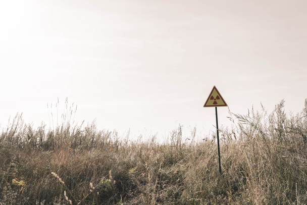 triángulo con símbolo tóxico de advertencia cerca del campo, concepto post apocalíptico
 - Foto, imagen