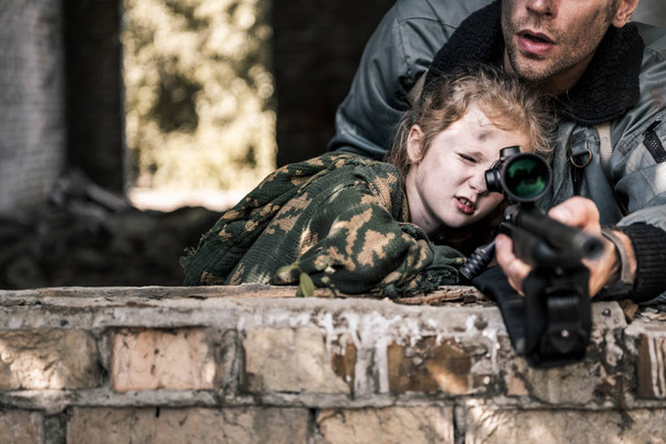 abgeschnittene Ansicht eines Mannes, der eine Waffe in der Nähe eines Kindes berührt, postapokalyptisches Konzept - Foto, Bild
