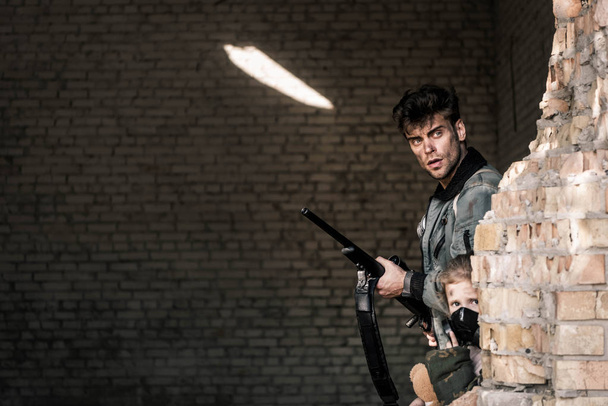 jóképű férfi kezében fegyver közel elhagyott épület, poszt apokaliptikus koncepció - Fotó, kép
