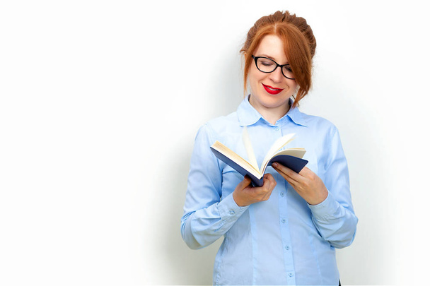 Woman holding open book in hands, redhead female in eyeglasses reading, enjoying interesting literature, novel or poetry, teacher working with textbook over gray background - Фото, зображення