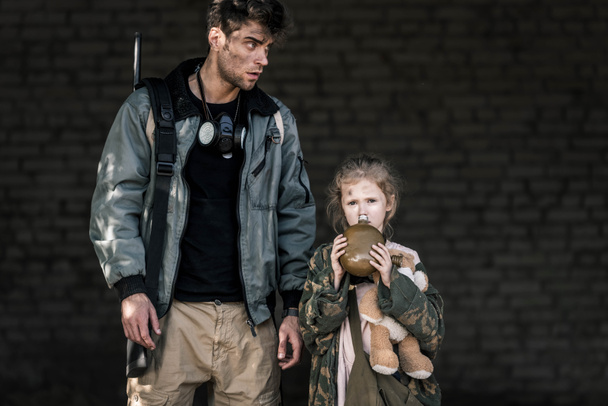 jóképű férfi áll gyerek mellett flaskával, poszt apokaliptikus koncepció - Fotó, kép