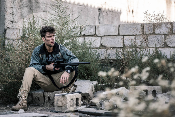 selektiver Fokus eines gutaussehenden Mannes mit Waffe in der Nähe einer Ziegelmauer, postapokalyptisches Konzept - Foto, Bild
