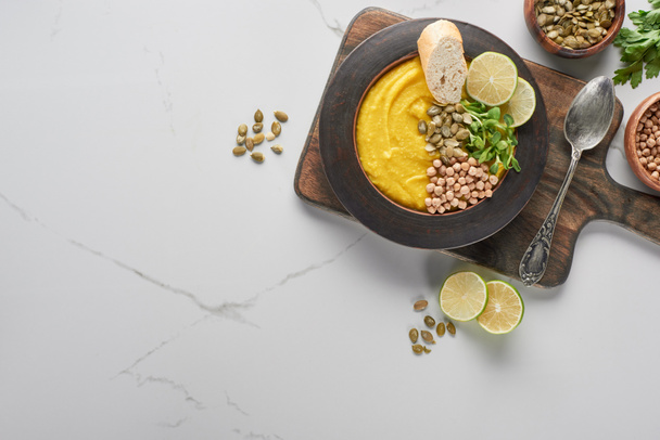 top view of autumnal mashed pumpkin soup in bowl on wooden cutting board with spoon on marble surface - Valokuva, kuva