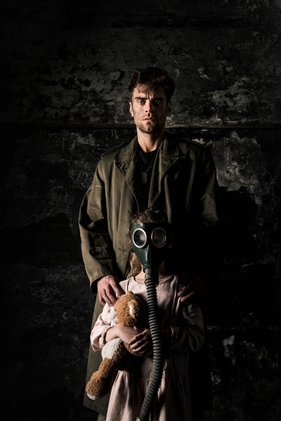 jóképű férfi áll gyerek mellett gázálarcos játékmackó, poszt apokaliptikus koncepció - Fotó, kép