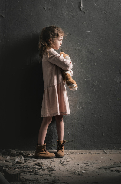 side view of kid holding soft toy near wall, post apocalyptic concept - Foto, Bild