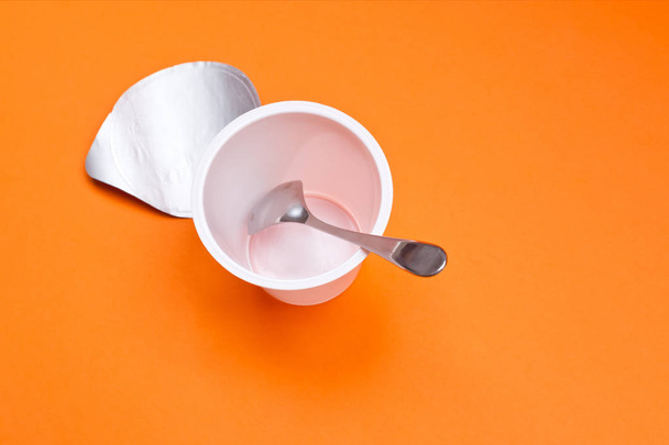 taza de yogur limpio vacío con cuchara sobre un fondo naranja
 - Foto, Imagen