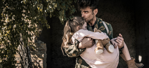 panoramic shot of man holding in arms and kissing kid with teddy bear, post apocalyptic concept - Photo, Image