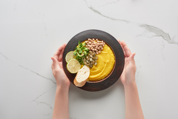 cropped view of woman holding autumnal mashed pumpkin soup on marble surface - Photo, Image