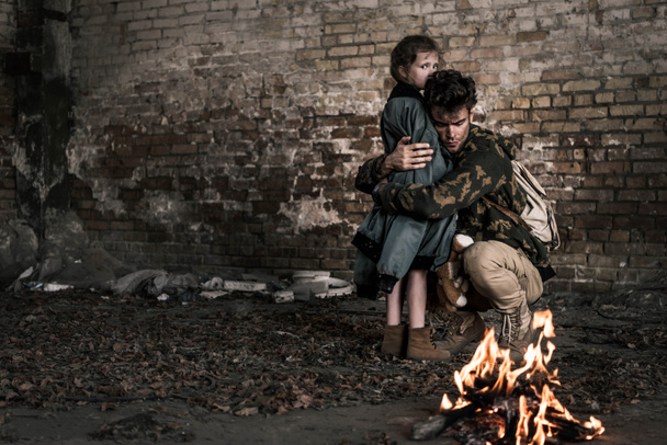 handsome man hugging child near burning bonfire, post apocalyptic concept - Fotó, kép