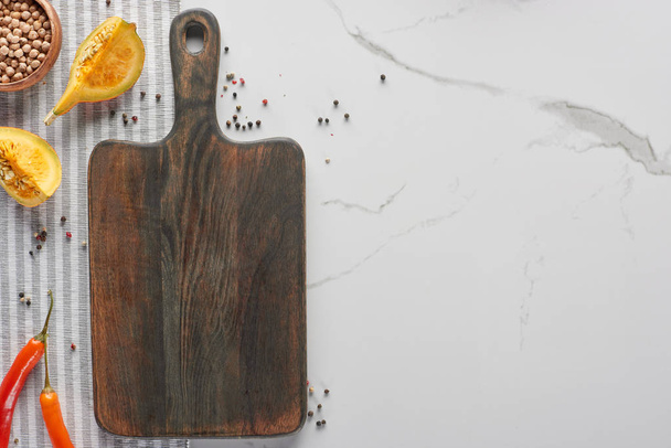 top view of wooden cutting board with pumpkin, chickpea and chili pepper on marble surface - Fotó, kép