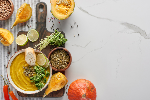 top view of seasonal mashed pumpkin soup on wooden cutting board with ingredients on marble surface - Photo, Image
