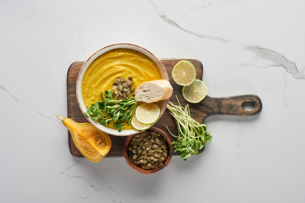вид сверху на вкусный суп из пюре из тыквы на деревянной доске для резки мрамора с ингредиентами
 - Фото, изображение