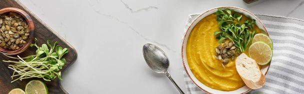 panoramic shot of tasty mashed pumpkin soup on wooden cutting board with ingredients on marble surface - Photo, Image