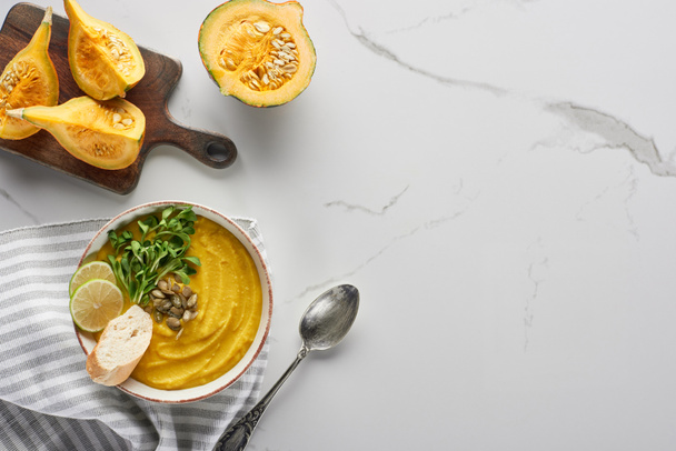 top view of tasty mashed pumpkin soup on wooden cutting board with ingredients on marble surface - Foto, afbeelding