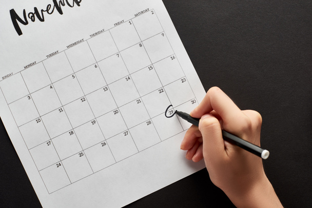 cropped view of woman marking black Friday date in calendar on black background - Photo, Image