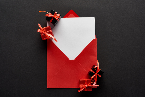 top view of blank card in red envelope near presents on black background - Фото, зображення