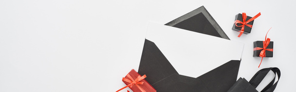 vue du dessus de l'enveloppe noire avec carte blanche près des boîtes-cadeaux décoratives et sac à provisions sur fond blanc, vue panoramique
 - Photo, image