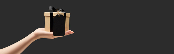 przycięty widok kobiety trzymającej pudełko z czarną, pustą etykietą w ręku odizolowaną na czarnym, panoramicznym ujęciu - Zdjęcie, obraz