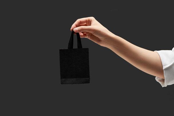 przycięty widok kobiety trzymającej małą czarną torbę na zakupy w ręku odizolowany na czarno - Zdjęcie, obraz