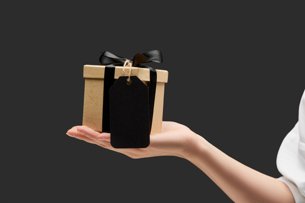 rajattu näkymä nainen tilalla lahjapakkauksessa musta tyhjä etiketti kädessä eristetty musta
 - Valokuva, kuva