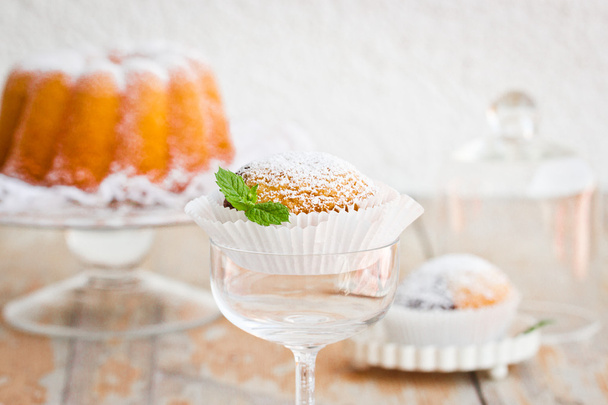 Little cupcake with powdered sugar and mint leaf on old wooden table - Photo, Image