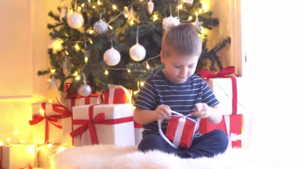 Attractive little boy unwrapping Christmas gifts. Kid opening New Year presents at home. - Felvétel, videó