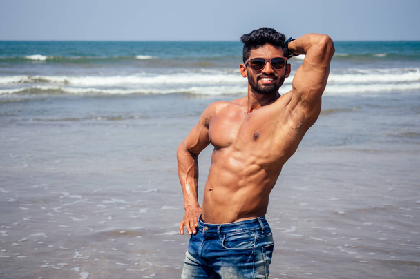 Топлес спортивний, м'язистий і здоровий чорний чоловік розігріває інструктора на пляжі.індійська модель чоловічої моди з джинсовими шортами та ідеальним тілом. здорове харчування та активні пляжні канікули
 - Фото, зображення