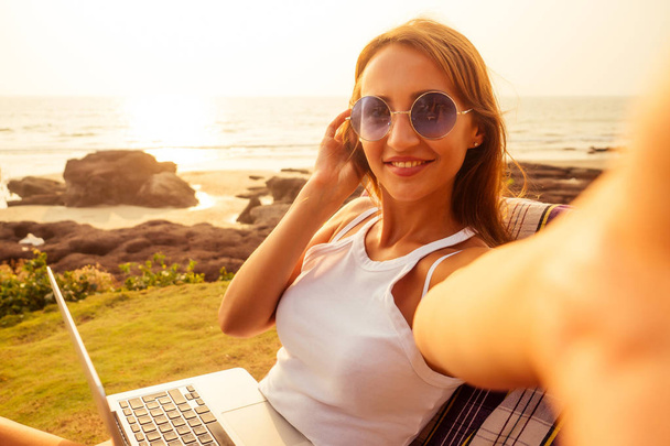 dziewczyna siedzi na pomarańczowym leżaku z laptopem nad morzem w ośrodku. piękna kobieta biznesu w stylowej strój kąpielowy bikini Coral mają sezonowe zimowe wakacje na plaży w egzotycznym kraju - Zdjęcie, obraz