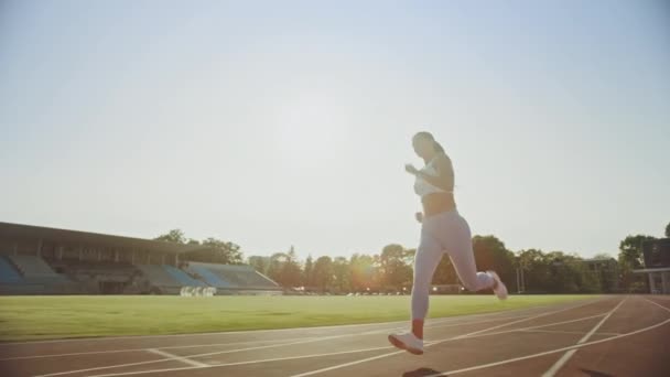 Beautiful Fitness Woman in Light Blue Athletic Top and Leggings is Starting a Sprint Run in an Outdoor Stadium. She is Running on a Warm Summer Day. Athlete Doing Her Sports Practice. Tracking Shot. - Materiał filmowy, wideo