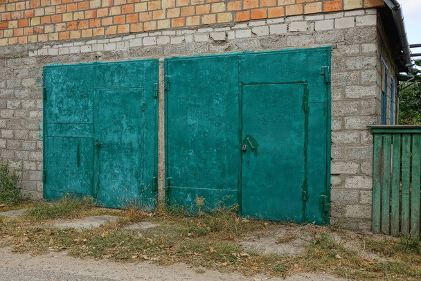 πρόσοψη ενός γκρι γκαράζ τούβλο με δύο σιδερένιες πράσινες πύλες στο δρόμο - Φωτογραφία, εικόνα