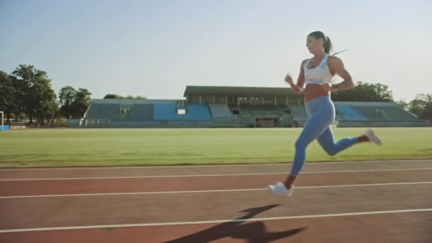 Beautiful Fitness Woman in Light Blue Athletic Top and Leggings Jogging in a Stadium. She is Running on a Warm Summer Afternoon. Athlete Doing Her Routine Sports Practice on a Track. Slow Motion. - Materiał filmowy, wideo