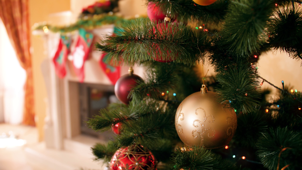 4k Nahaufnahme Video der Kamera langsam Schwenk über schönen Weihnachtsbaum mit bunten Kugeln und leuchtenden Lichterketten im Wohnzimmer zu Hause dekoriert - Filmmaterial, Video