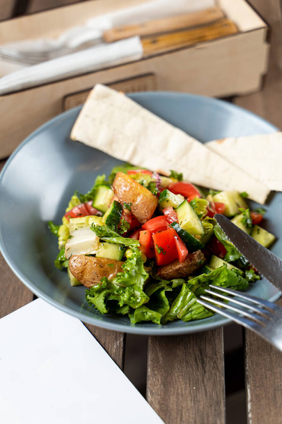 Salade de saison chaude avec veste de pommes de terre cuite au four, servie avec pain plat sur une table en bois
 - Photo, image