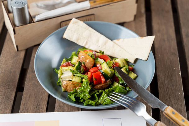 Teplý sezonní salát se salátovou bramborou, podávaný s plochým chlebem na dřevěném stole - Fotografie, Obrázek