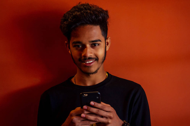 Biometric verification. Human facial detection, high technology. Indian man student holding phone face ID scanning orange wall background - Foto, afbeelding