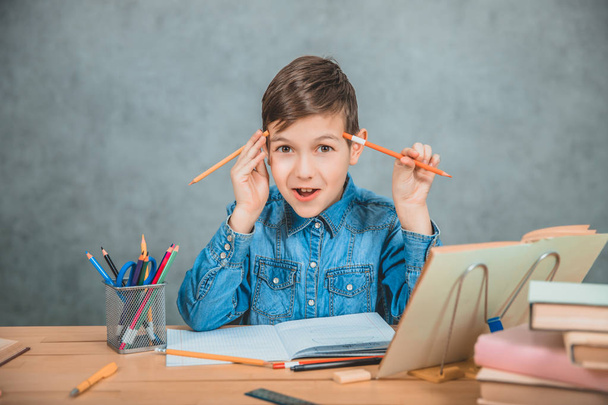 Ένα μικρό χαρούμενο παιδί που παίζει με μολύβια κατά τη διάρκεια της μάθησης. Στοίβα από βιβλία και pecils στο γραφείο. - Φωτογραφία, εικόνα
