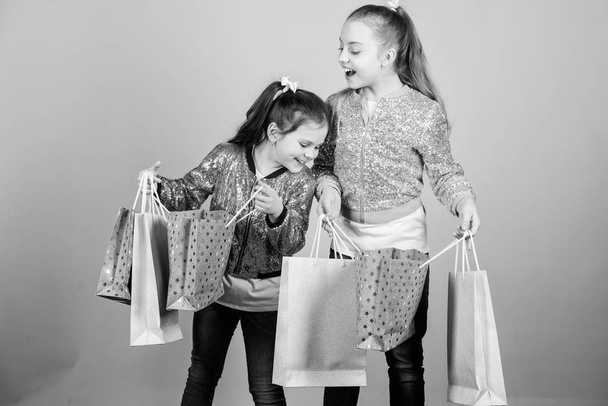 販売と割引。買い物の日。子供たちは束のパッケージを持っています。キッズファッション。より多くを期待してください。より少ない支払い。女の子の姉妹は、ショッピングバッグベージュの背景を持つ友人。買い物と購入。ブラックフライデー - 写真・画像