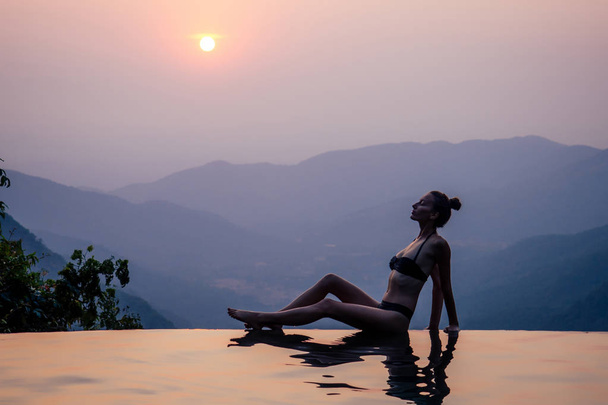 Young woman relaxing in infinity swimming pool looking at view romantic sunset overlooking the hills wildernest nature spa resort in India Goa Kerala - Foto, Bild