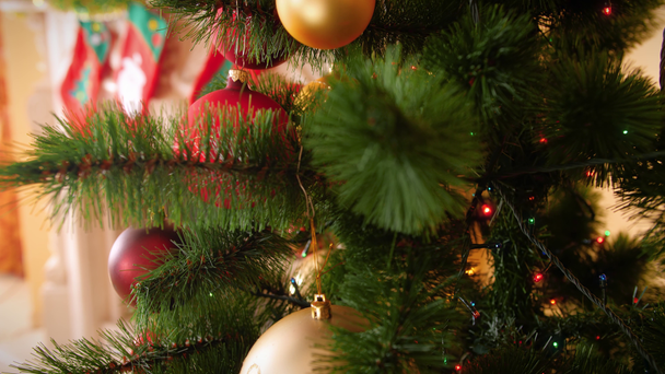 カメラのクローズアップ4k映像は、リビングルームでクリスマスツリーにカラフルなボーブルと輝く光の花輪をゆっくりと上に移動します。あなたの冬の休日やお祝いのための完璧なショット - 映像、動画