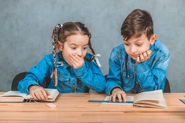 Smart boy and girl totally involved in the process of reading. Boy is pointing at something interesting in his book. Girl is surprised, covering her mouth with a hand. - 写真・画像