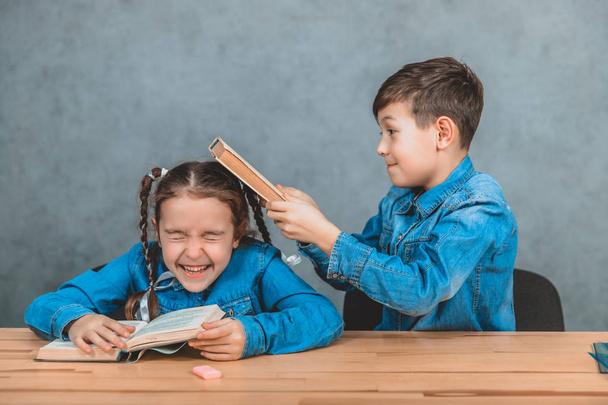 Naughty little schoolboy is hitting lovely schoolgirl in her head with a book. Fight. - Φωτογραφία, εικόνα