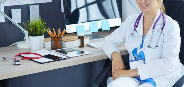 Portrait of young female doctor sitting at desk in hospital - 写真・画像