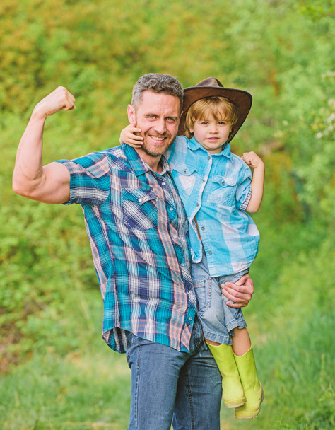 kid in rubber boots. happy dad in forest. human and nature. family day. happy earth day. Eco farm. small boy help muscular father in farming. father and son in cowboy hat on ranch. stronger together - Foto, immagini