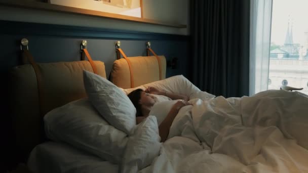 Привлекательная молодая женщина спит в гостиничном номере рано утром, лежа в постели
 - Кадры, видео