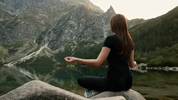 Zdrowa młoda kobieta medytuje na górskim jeziorze, praktykując jogę, cieszy się ciszą wysoko w górach - Materiał filmowy, wideo