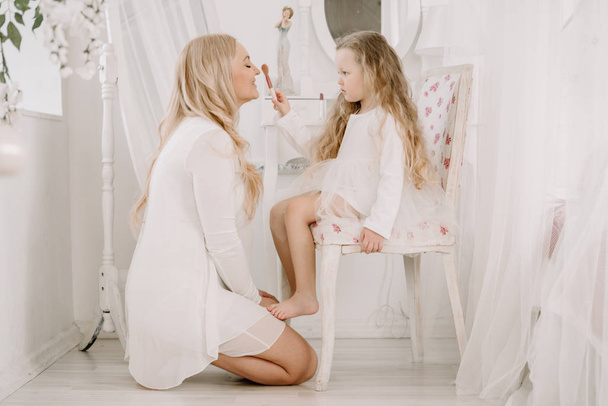 Όμορφη γυναίκα και παιδί κορίτσι που κάνουν το ένα το άλλο στο λευκό φόντο δωμάτιο - Φωτογραφία, εικόνα