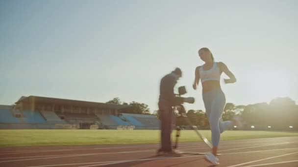 Beautiful Fitness Woman in Light Blue Athletic Top and Leggings Running Extremely Fast in an Outdoors Stadium. She is Sprinting on a Warm Summer Afternoon. Athlete Doing Her Sports Practice on a Track - Materiaali, video